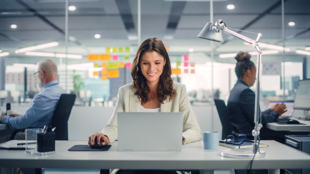 Young,Happy,Businesswoman,Using,Computer,In,Modern,Office,With,Colleagues.